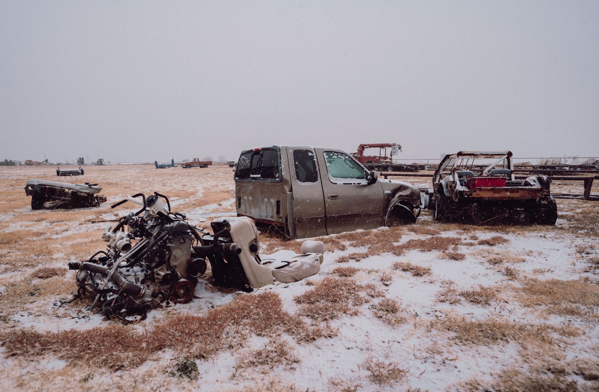 A snowy field scattered with abandoned and wrecked vehicles and parts.