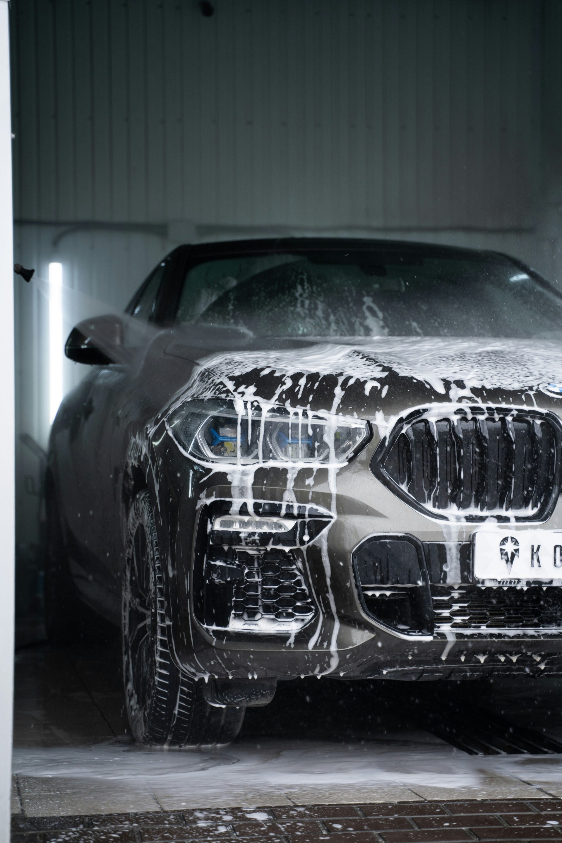 A grey car covered in white soap suds during a professional car wash